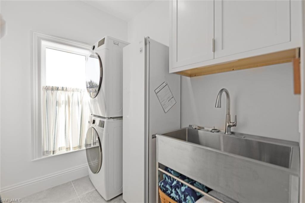 Laundry area featuring a healthy amount of sunlight, stacked washing maching and dryer, sink, and light tile patterned floors