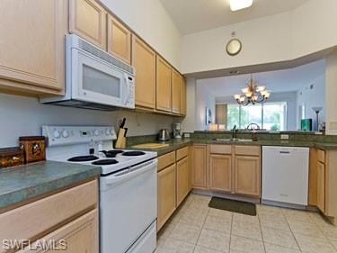 Kitchen with white appliances, a chandelier, dark countertops, light tile patterned floors, and light brown cabinets