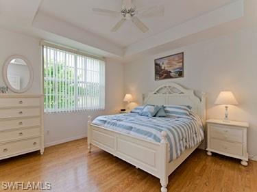 Bedroom with a raised ceiling, a ceiling fan, and light wood-style floors