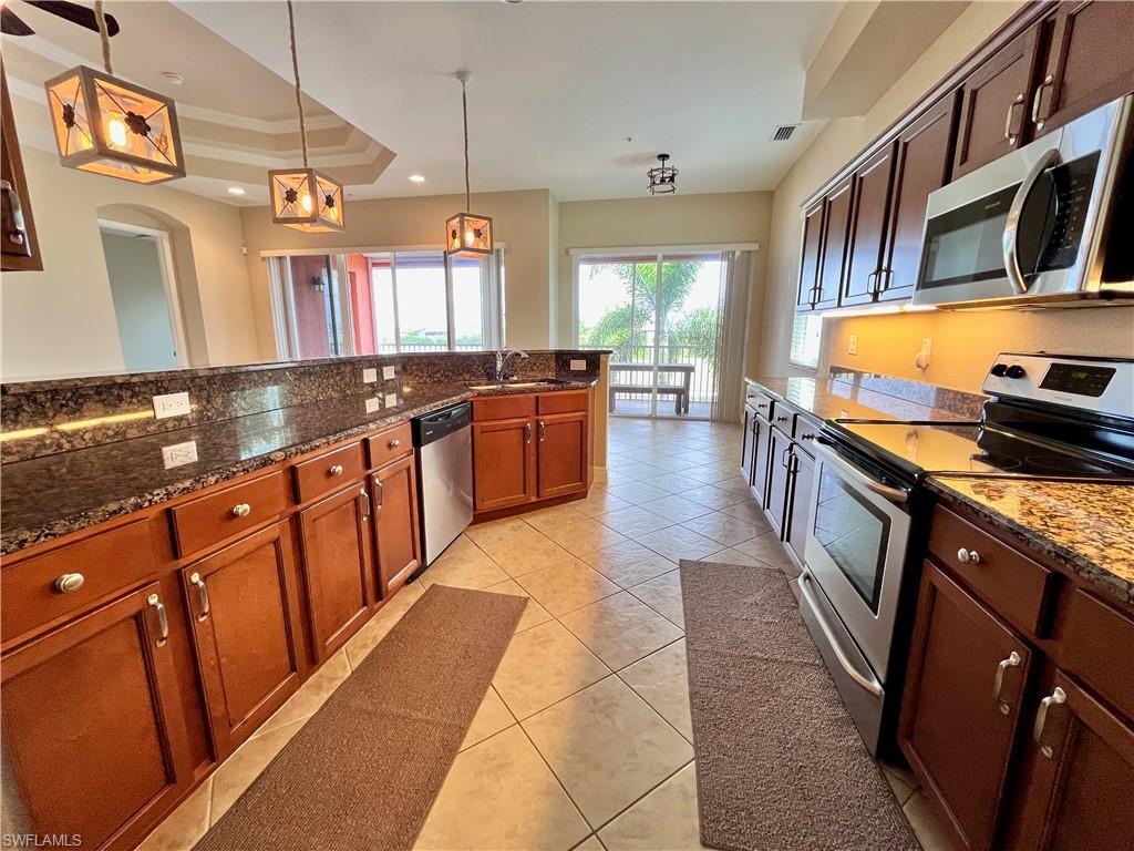 Kitchen featuring stainless steel appliances, pendant lighting, dark stone countertops, a raised ceiling, and light tile patterned floors