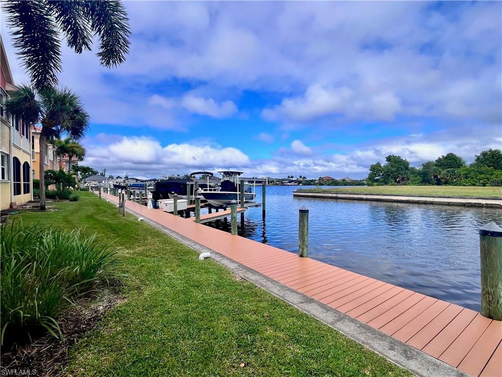 Dock with a lawn, a water view, and boat slip with lift and electric and water at the dock