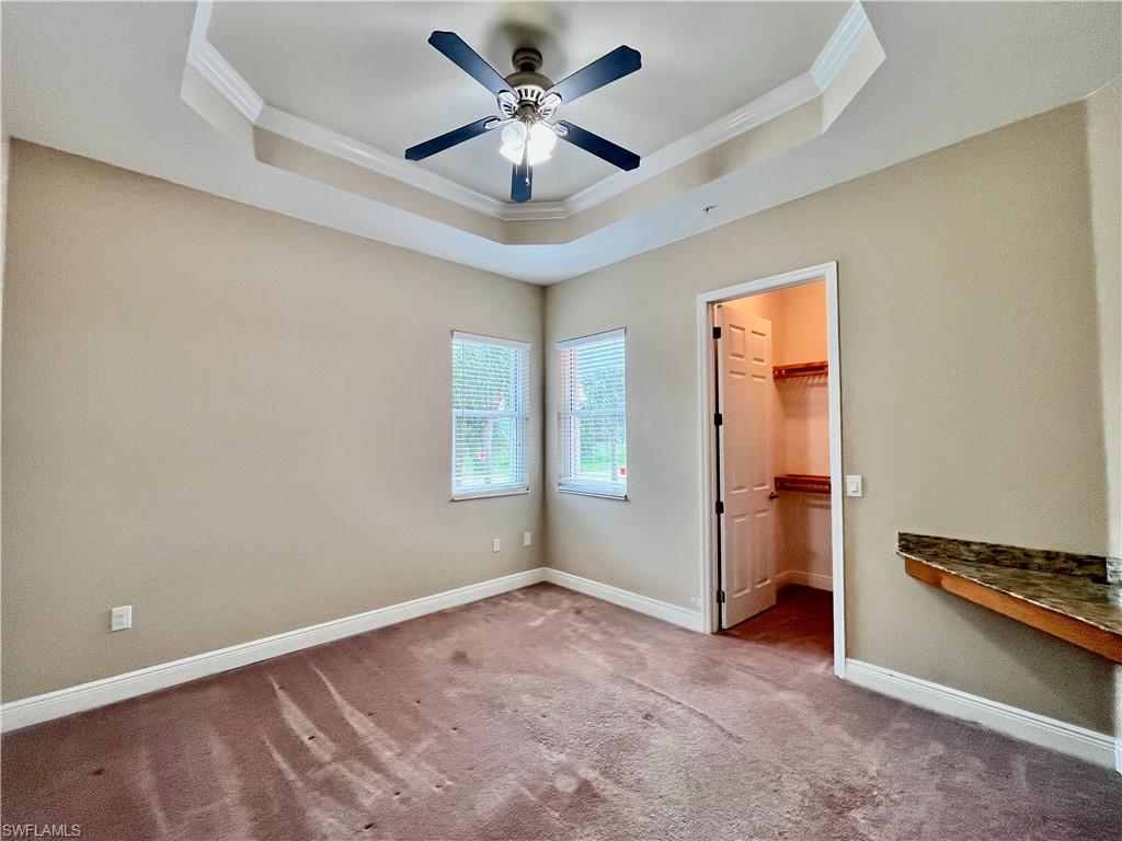 Bedroom #3 with a walk in closet, crown molding, a tray ceiling, carpet floors, and a ceiling fan