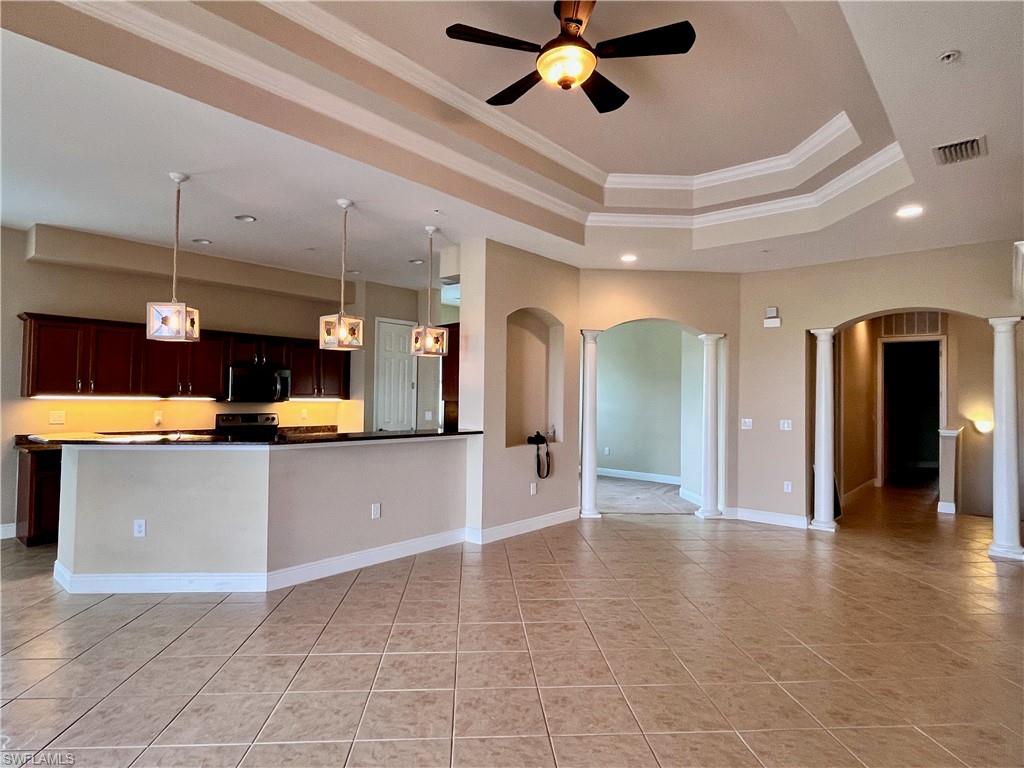 Kitchen featuring crown molding, hanging light fixtures, a tray ceiling, dark countertops, and open floor plan