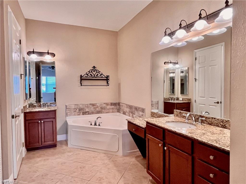Primary Bathroom with two vanities, a jetted bath tub, and light tile floors, his and her walk in closets