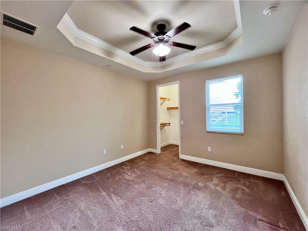 Bedroom #2 with walk in closet, natural light, hurricane windows and shutters, featuring ornamental molding, carpet flooring, a raised ceiling and ceiling fan