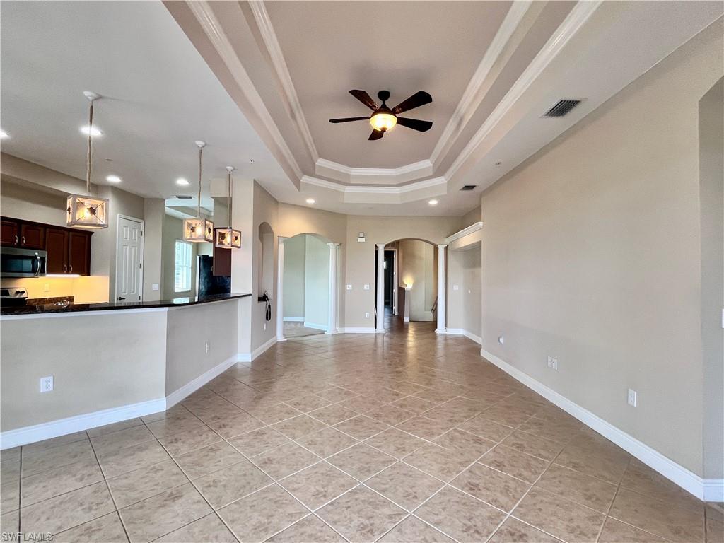 Large living room with dry bar area, eat in area,  crown molding, arched walkways, light tile patterned floors, a tray ceiling, and ceiling fan