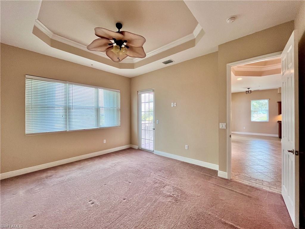 Primary bedroom with ensuite bathroom, his and her walk in closets with a tray ceiling, light colored carpet, crown molding, and a ceiling fan