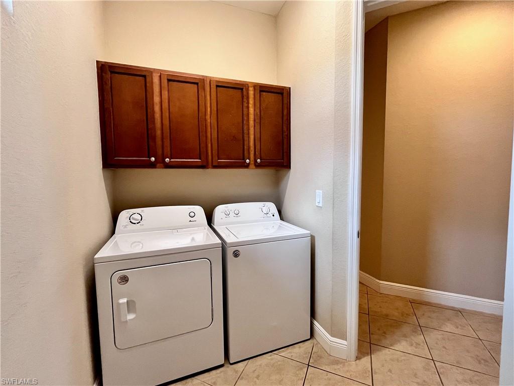 Laundry area featuring light tile patterned flooring, washing machine and clothes dryer, and cabinet space