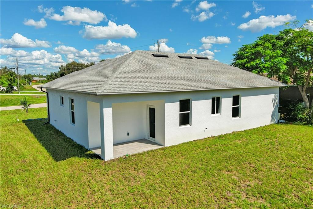 Back of property featuring a lawn, roof with shingles, stucco siding, and a patio area