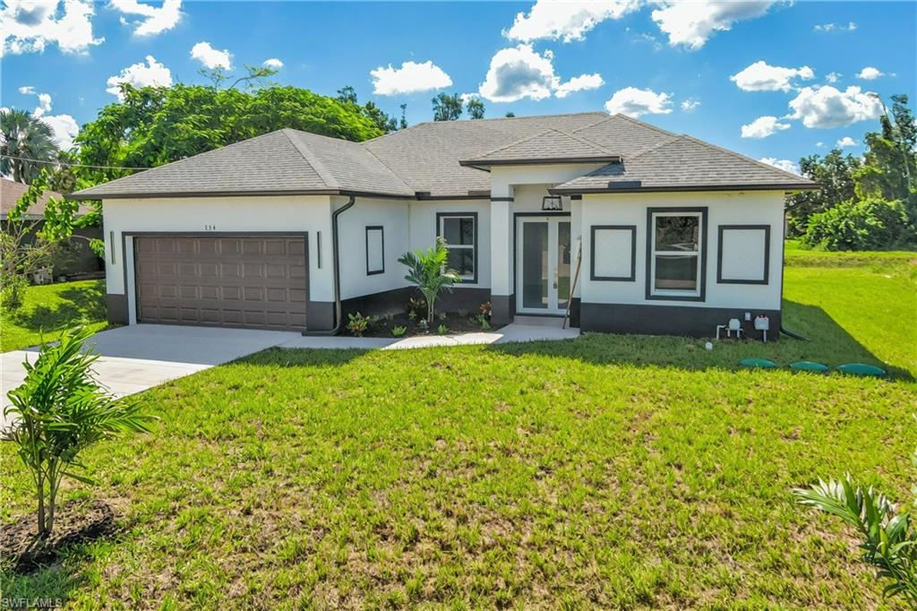 View of front of property featuring stucco siding, driveway, a front lawn, a garage, and french doors