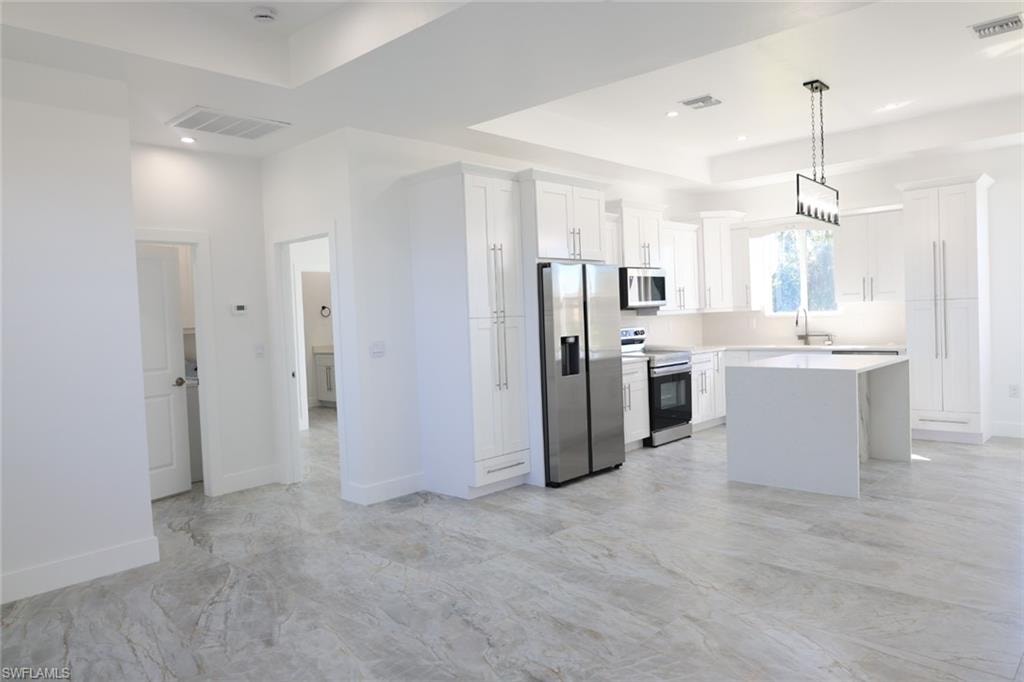 Kitchen with a center island, stainless steel appliances, white cabinets, and a raised ceiling