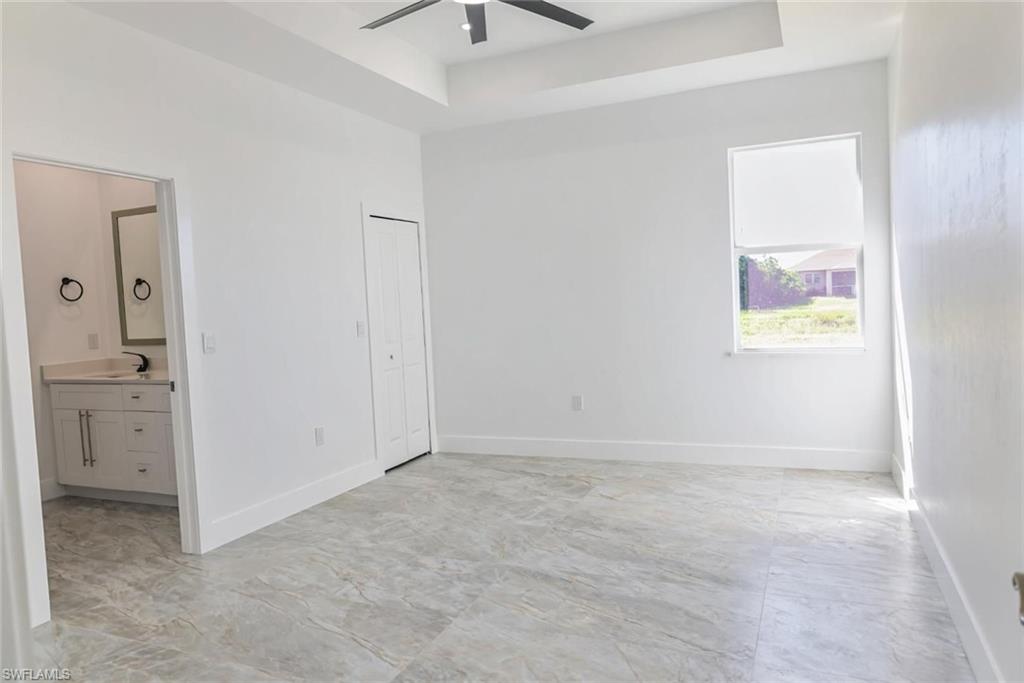 Unfurnished bedroom featuring a tray ceiling, ceiling fan, and ensuite bathroom
