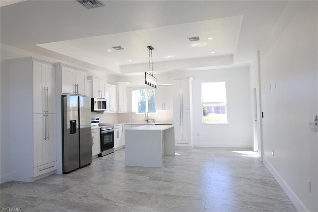 Kitchen with a tray ceiling, stainless steel appliances, white cabinets, and recessed lighting