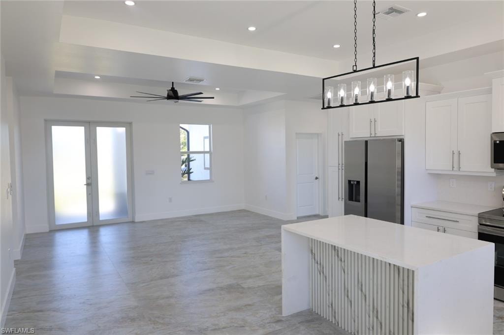 Kitchen with a raised ceiling, appliances with stainless steel finishes, white cabinetry, hanging light fixtures, and recessed lighting