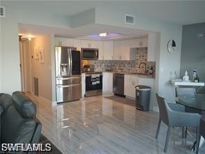 Kitchen with appliances with stainless steel finishes, tasteful backsplash, open floor plan, light countertops, and white cabinetry