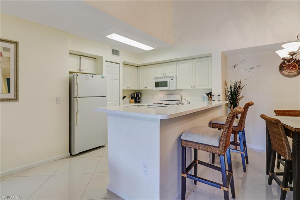 Kitchen featuring white appliances, light countertops, light tile patterned floors, a peninsula, and a breakfast bar area
