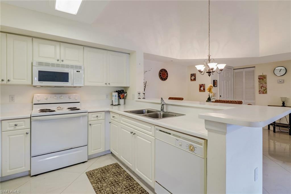 Kitchen featuring white appliances, light countertops, white cabinets, light tile patterned flooring, and decorative light fixtures