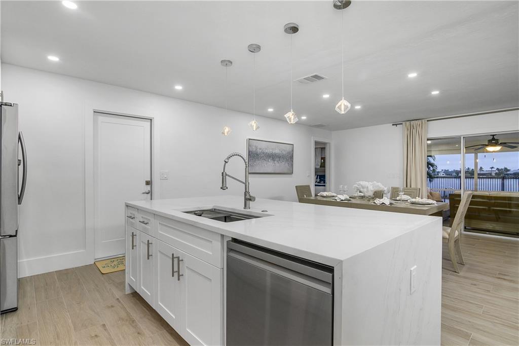 Kitchen with stainless steel appliances, pendant lighting, light wood-style floors, light stone counters, and recessed lighting