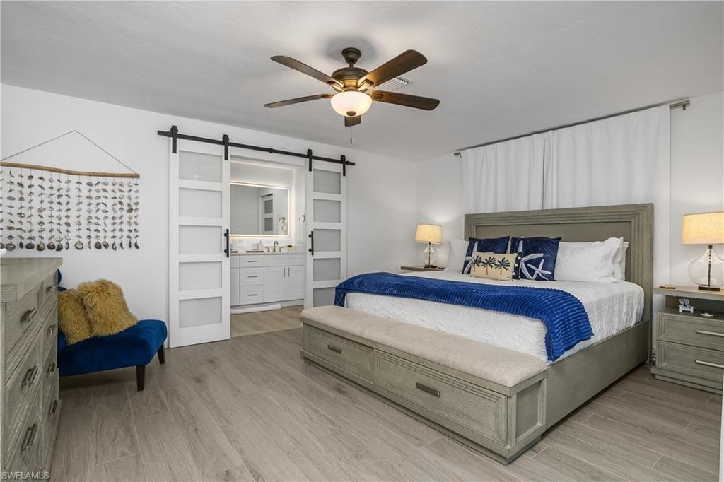 Bedroom with a barn door, wood finished floors, a ceiling fan, and connected bathroom
