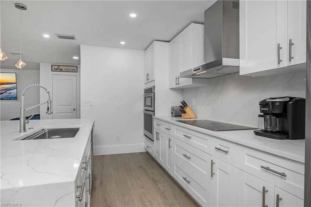 Kitchen with wall chimney range hood, light stone countertops, pendant lighting, light wood-type flooring, and recessed lighting