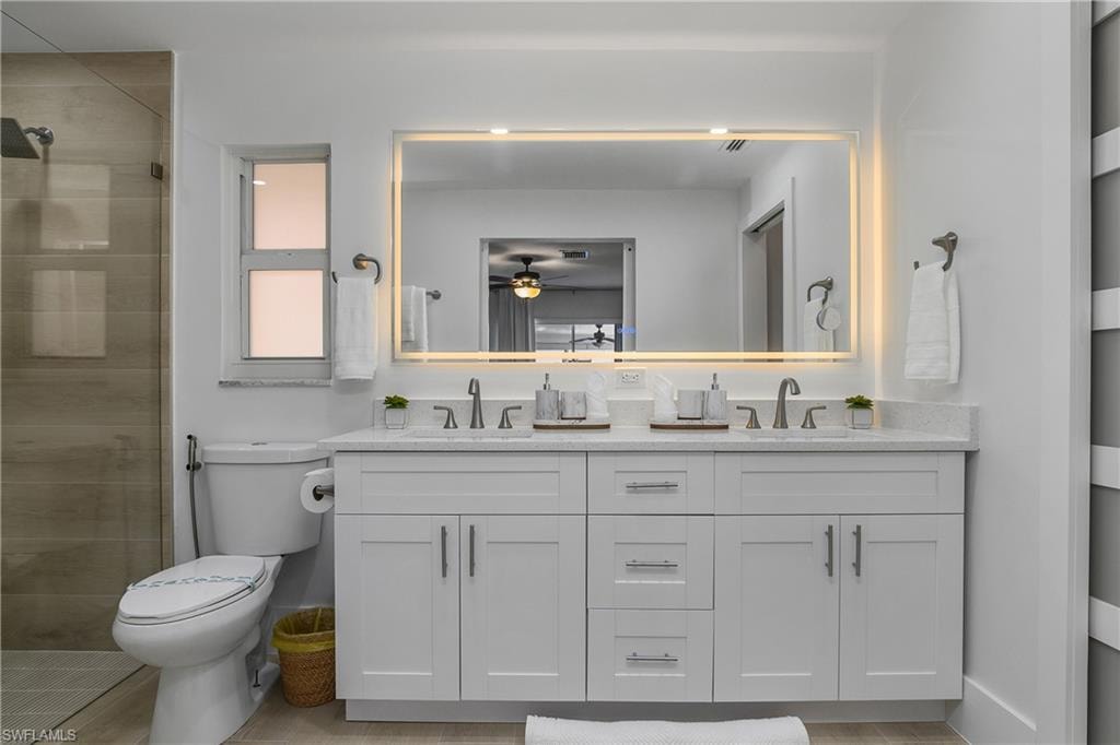 Full bathroom with double vanity, tiled shower, a ceiling fan, and light tile patterned floors