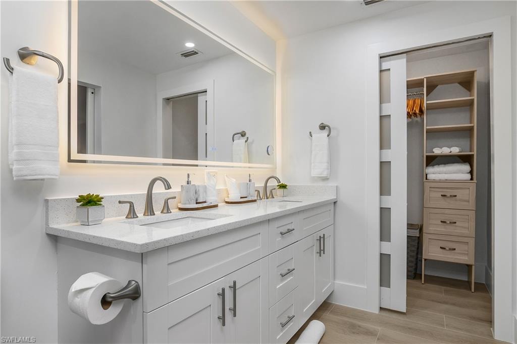 Bathroom with double vanity, wood finish floors, recessed lighting, and a walk in closet