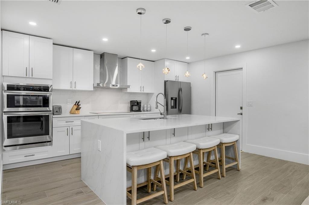 Kitchen featuring wood tiled floors, a kitchen bar, decorative light fixtures, light stone countertops, and recessed lighting