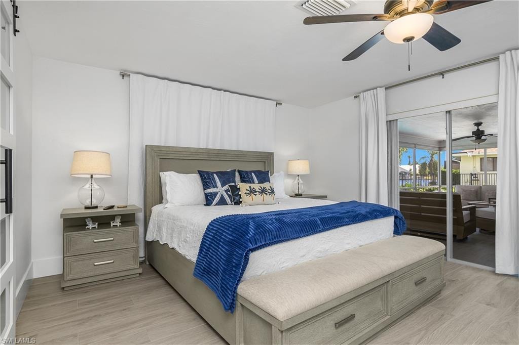 Bedroom with access to outside, light wood-style floors, ceiling fan, and a barn door