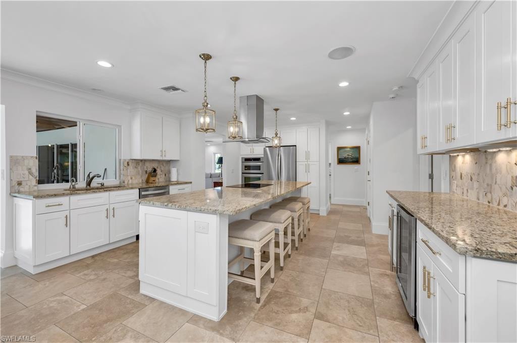 Kitchen featuring tasteful backsplash, hanging light fixtures, light stone counters, a kitchen island, and a breakfast bar area