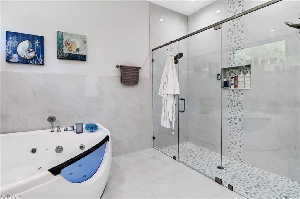 Full bathroom featuring tile walls, a shower stall, a whirlpool tub, and tile patterned floors