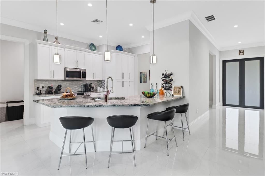 Kitchen with a peninsula, a breakfast bar, decorative backsplash, white cabinets, and stainless steel microwave