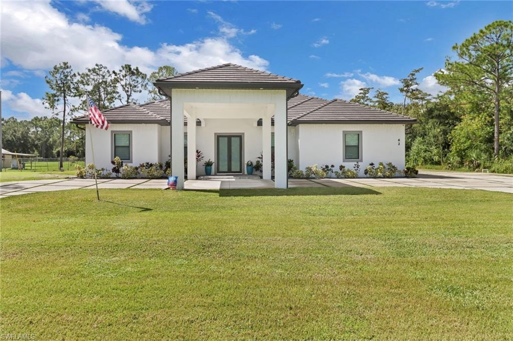 Front property with a yard, covered porch, a tiled roof, and stucco siding
