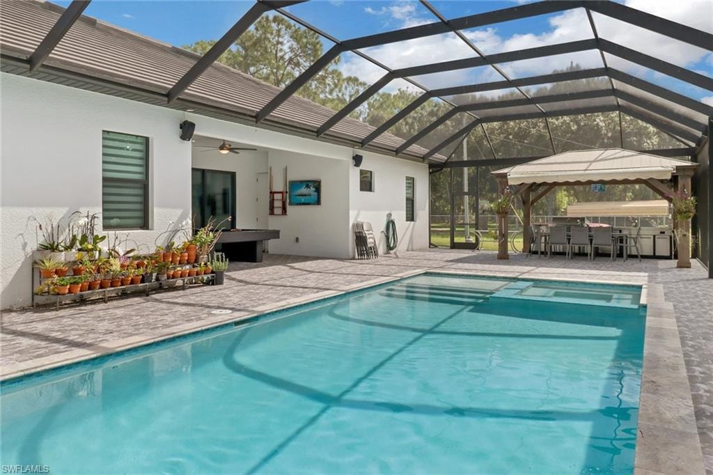 View of pool with a patio area, a lanai, a ceiling fan, and a pool with connected hot tub