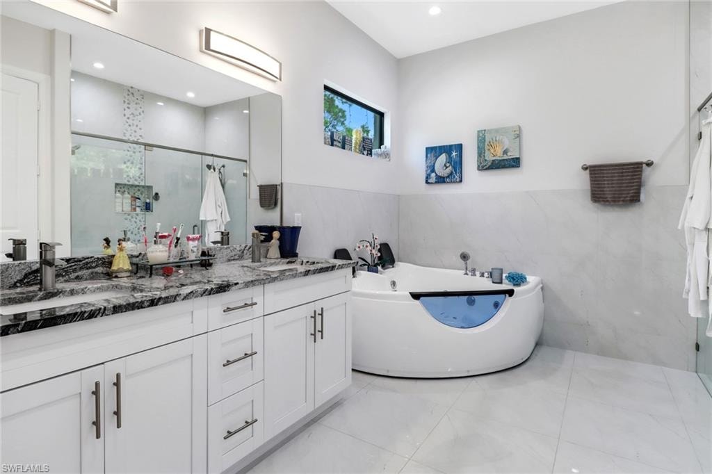 Full bathroom featuring double vanity, a tub with jets, a shower stall, tile walls, and wainscoting
