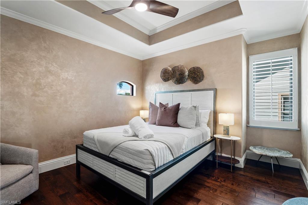 Bedroom featuring dark wood-style flooring, a raised ceiling, crown molding, and ceiling fan