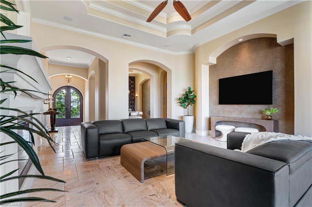 Living room featuring crown molding, stone tile flooring, a raised ceiling, arched walkways, and a ceiling fan