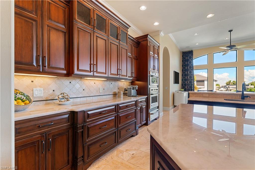 Kitchen with ceiling fan, arched walkways, light stone countertops, glass insert cabinets, and tasteful backsplash
