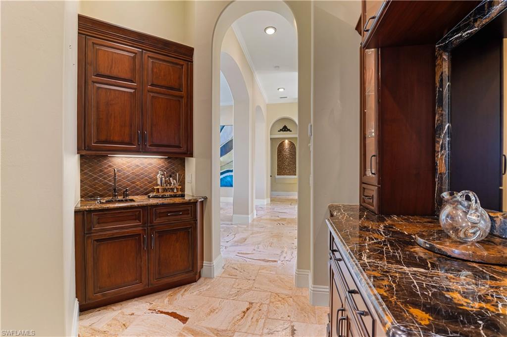 Indoor wet bar with arched walkways, dark stone counters, decorative backsplash, crown molding, and recessed lighting