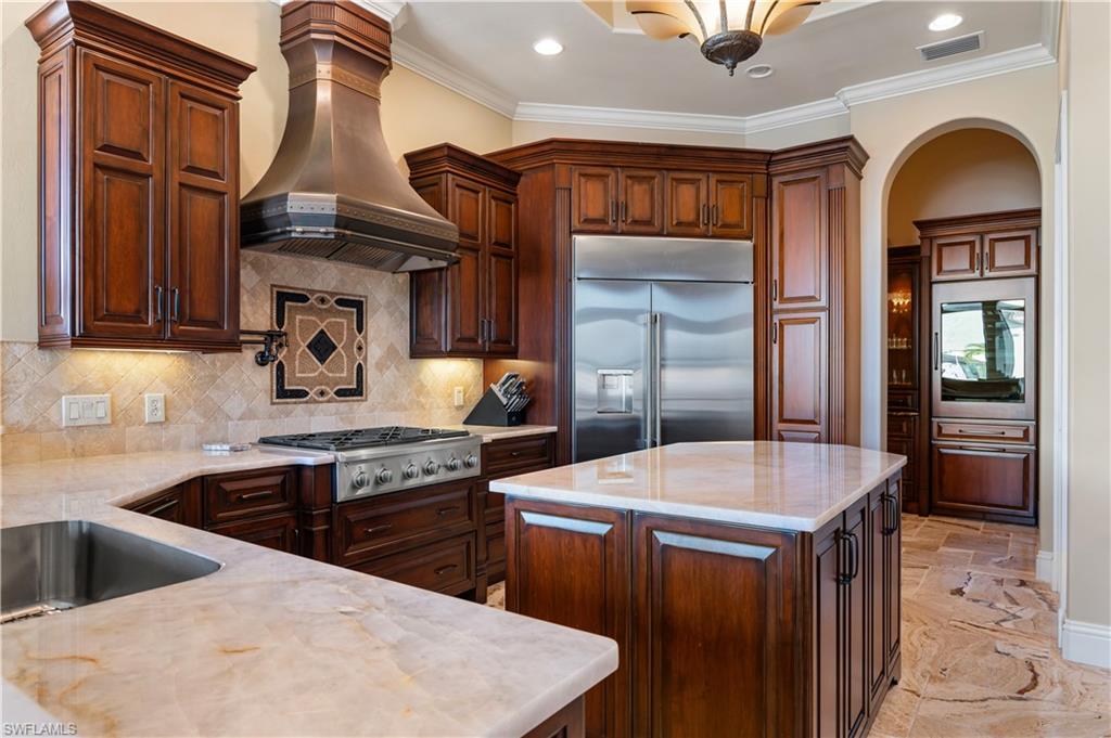 Kitchen with a kitchen island, decorative backsplash, stainless steel appliances, custom exhaust hood, and light stone countertops