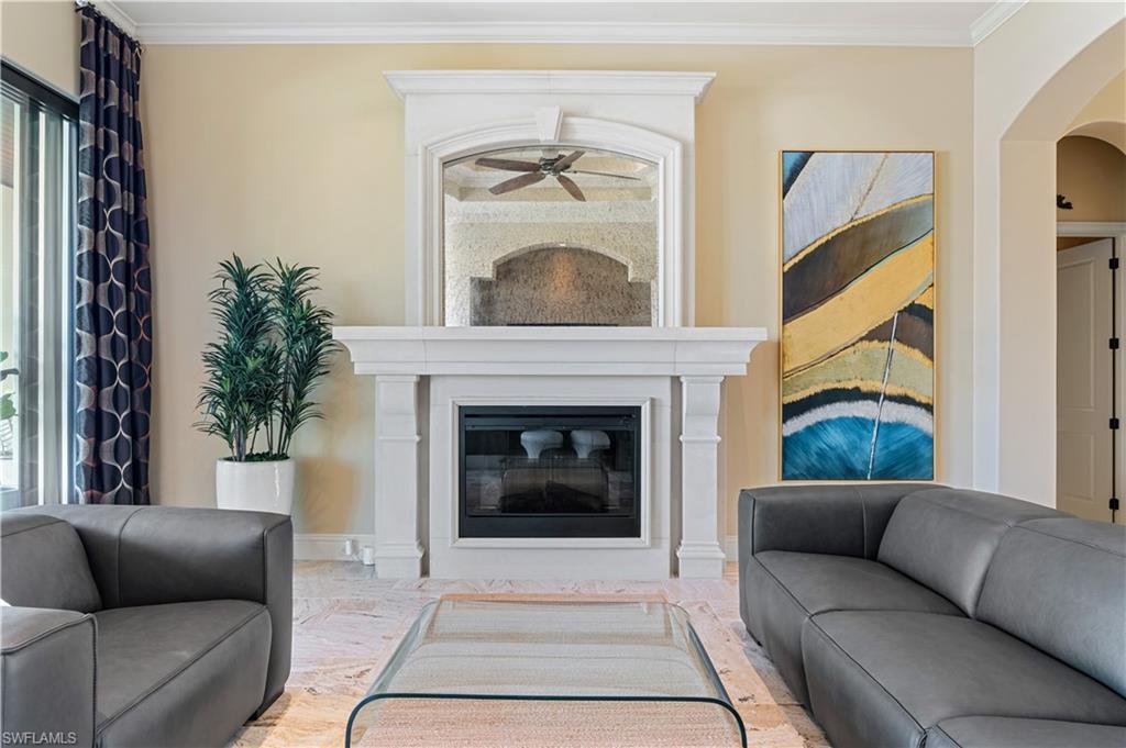 Living room with crown molding, a glass covered fireplace, plenty of natural light, arched walkways, and a ceiling fan