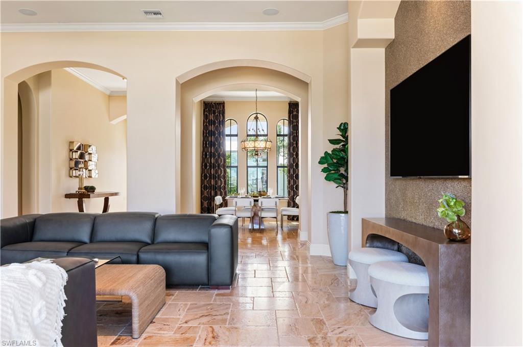 Living area with arched walkways, ornamental molding, a chandelier, and stone tile flooring