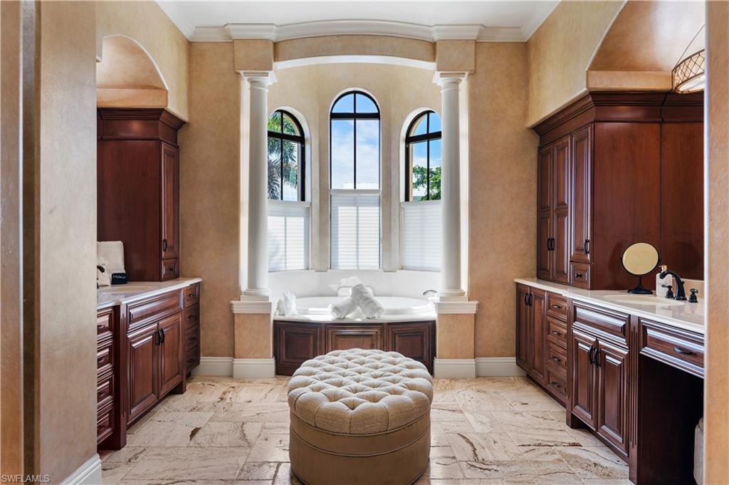 Bathroom with decorative columns, two vanities, crown molding, and a bath