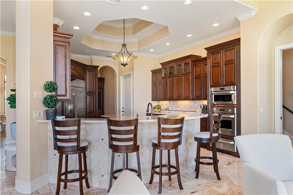 Kitchen featuring arched walkways, a raised ceiling, a breakfast bar, a peninsula, and recessed lighting