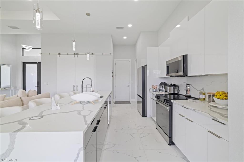 Kitchen with modern cabinets, decorative light fixtures, appliances with stainless steel finishes, light stone countertops, and white cabinets
