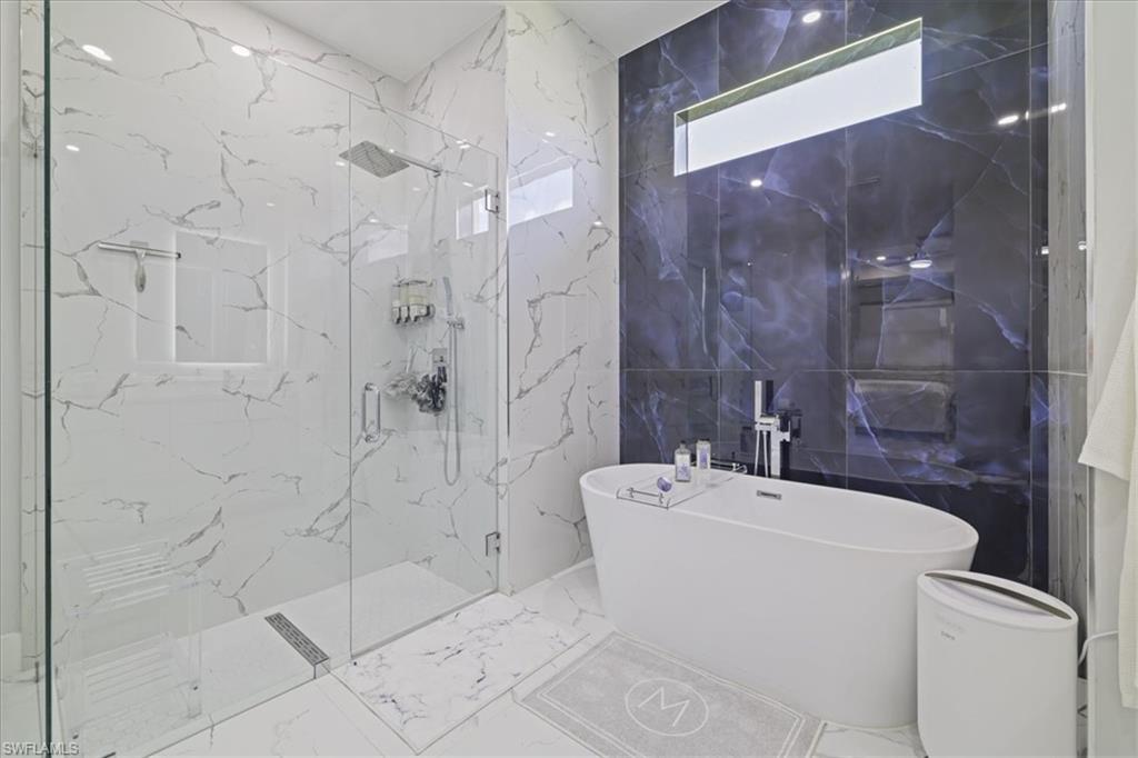 Bathroom featuring stone wall, a freestanding bath, marble tiled floors, a marble finish shower, and tile walls