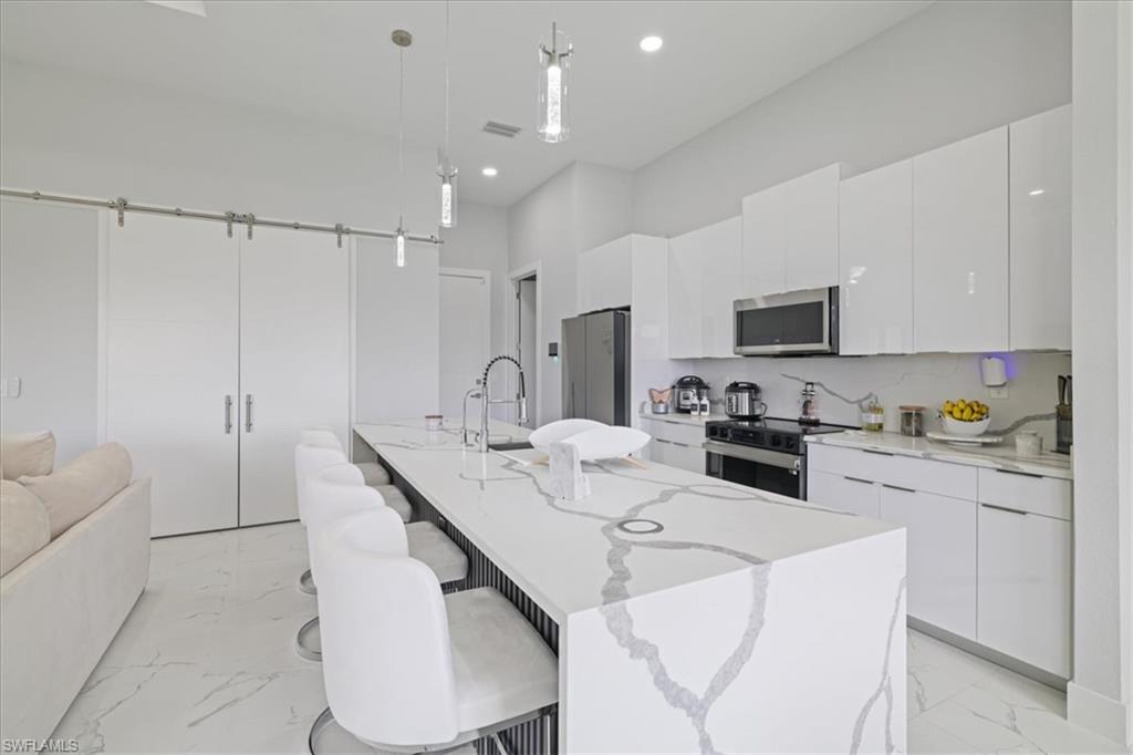 Kitchen featuring a kitchen breakfast bar, modern cabinets, pendant lighting, light marble finish floors, and white cabinets