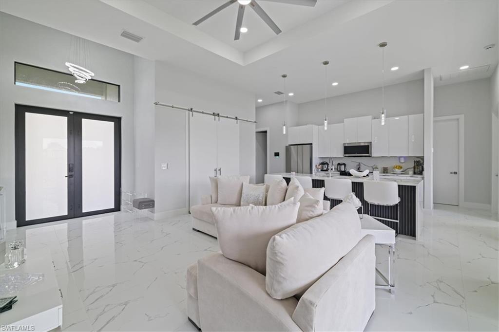 Living room featuring a barn door, light marble finish floors, french doors, a towering ceiling, and a ceiling fan