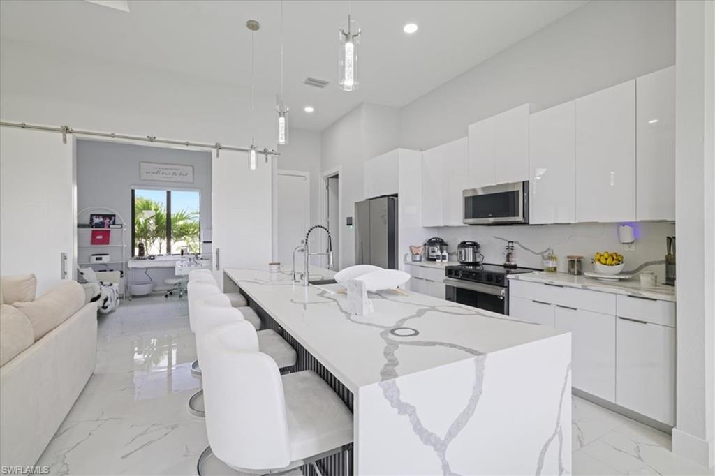 Kitchen featuring light marble finish flooring, a kitchen bar, open floor plan, pendant lighting, and recessed lighting
