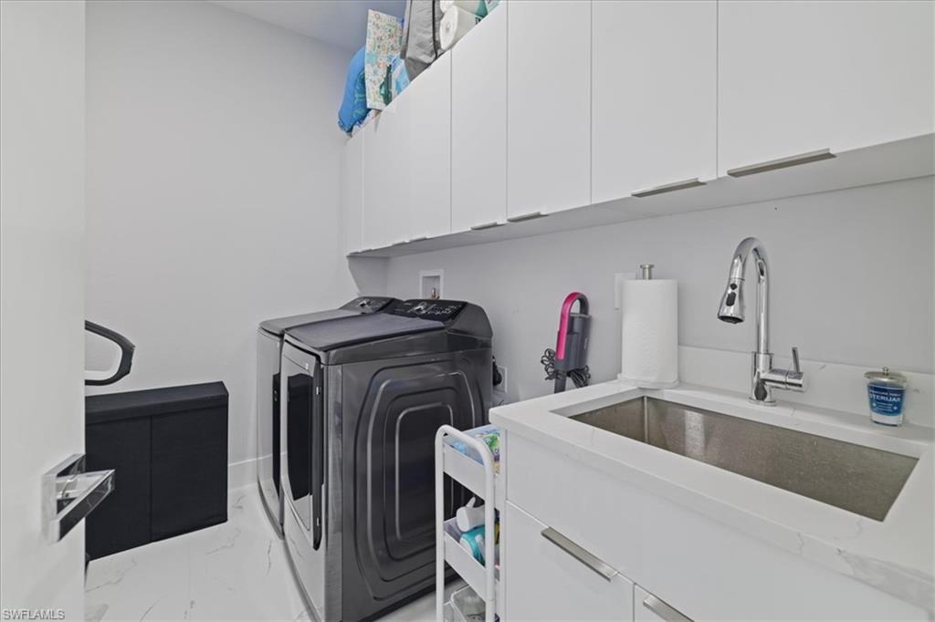 Washroom featuring light marble finish floors, cabinet space, and washing machine and dryer