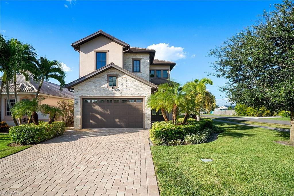 View of front of home featuring stone siding, a front yard, decorative driveway, a garage, and stucco siding